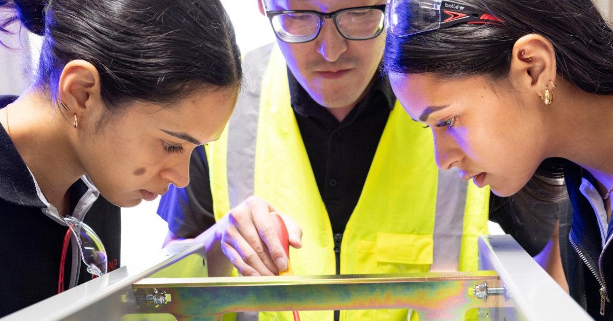 Apprentices learning with supervisor working on equipment in electrical workshop in New Zealand