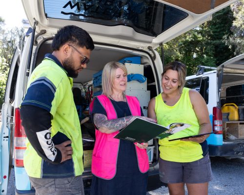 Apprentices and mentor reviewing paperwork beside a work van.